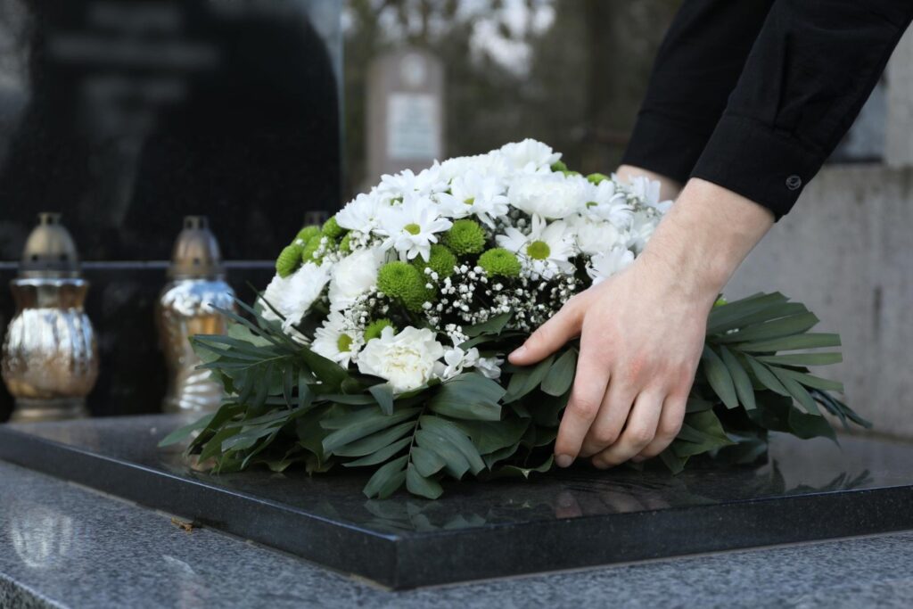 Woman putting funeral wreath of flowers on granite tombstone