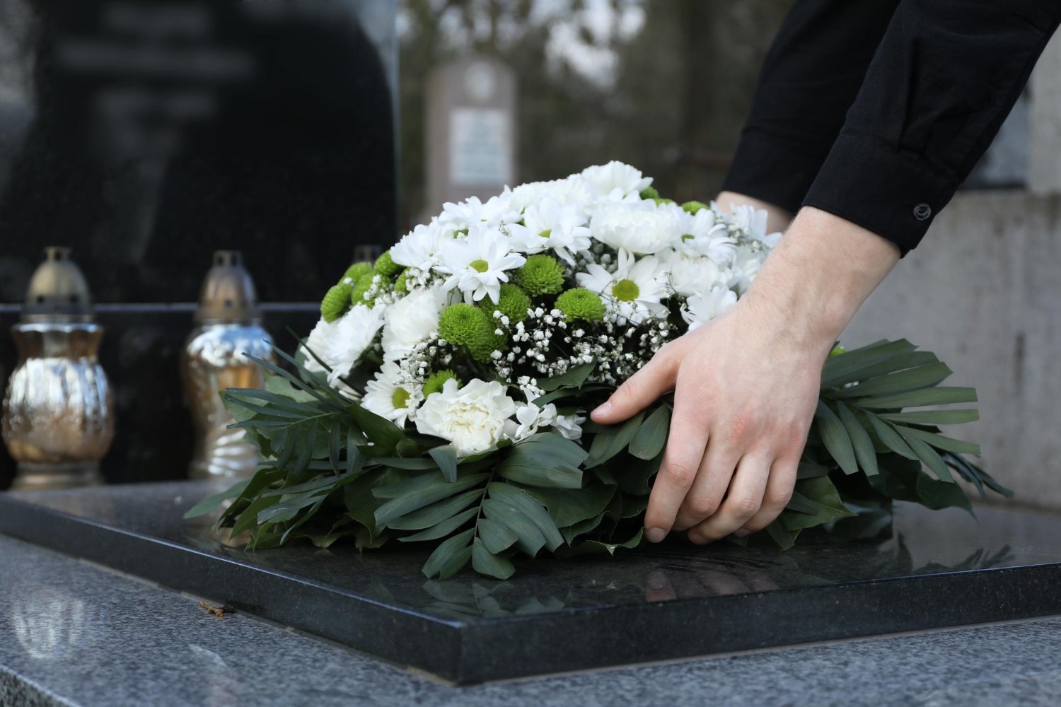 Woman putting funeral wreath of flowers on granite tombstone